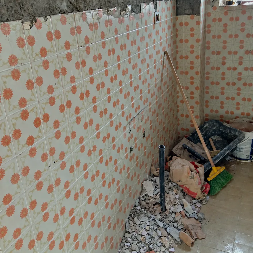 Casa de banho com azulejos antigos às flores e entulho no chão.